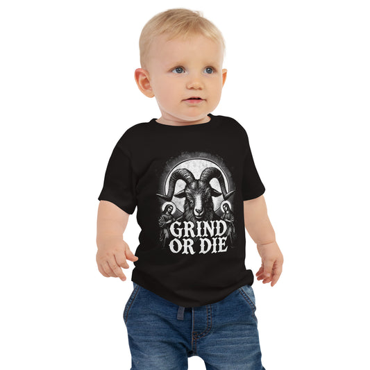 A toddler in a Bougie Boiz Club Grind Or Die baby t-shirt, featuring a white rams head graphic, stands against a plain white background. With short blonde hair and blue jeans, this determined little lifter already exudes style.