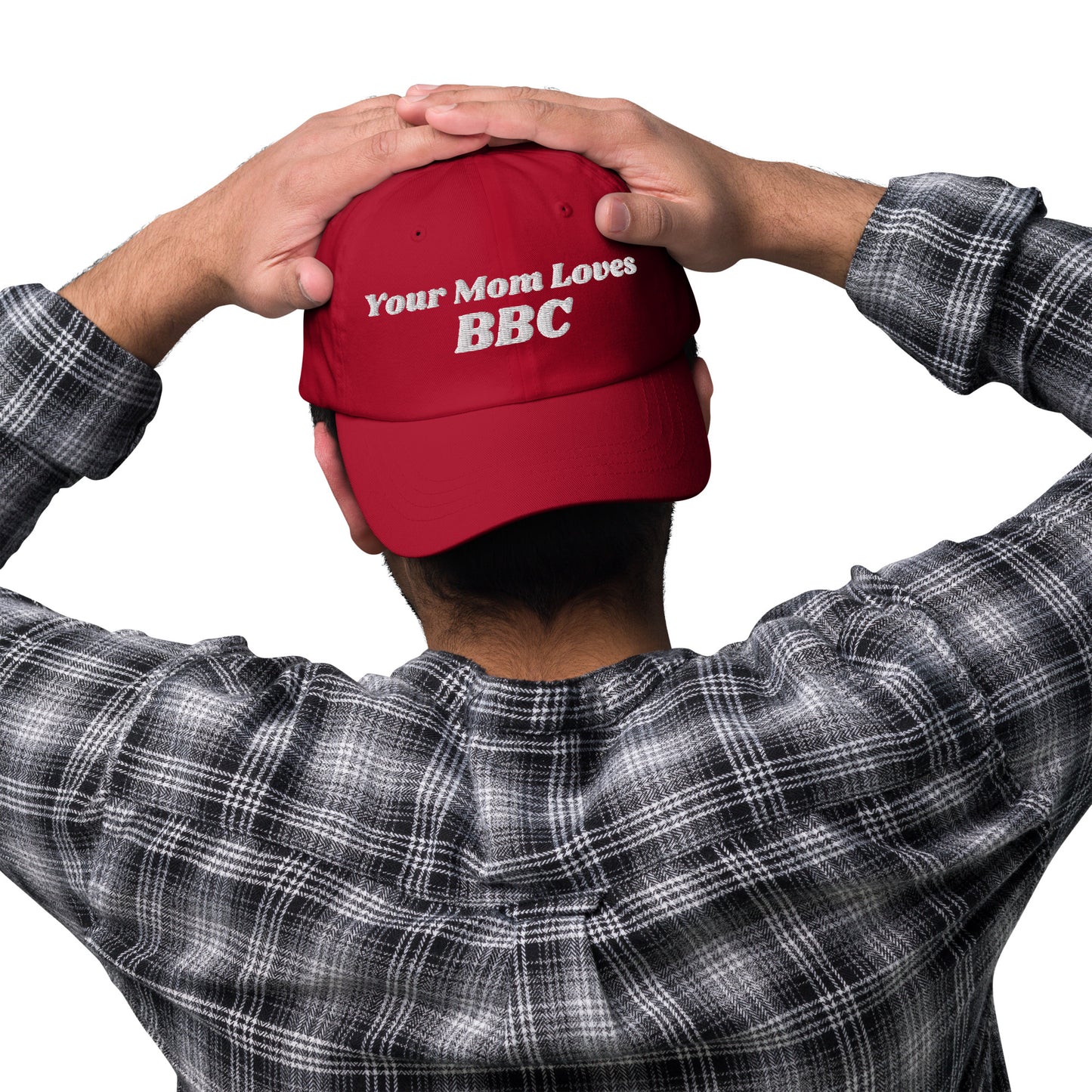 A person wearing a Bougie Boiz Clubs Your Mom Loves BBC embroidered hat, hands resting on the cap. Dressed in a black and white plaid shirt, they are viewed from behind against a simple background.