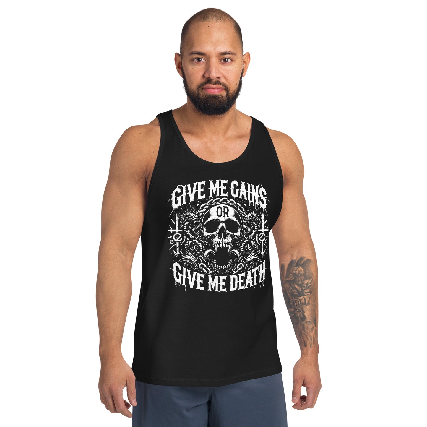 A bearded man embraces the iron life in a Bougie Boiz Club Give Me Gains - Tank Top featuring a skull graphic. Against a plain white backdrop, he pairs this black top with blue shorts, exuding serious gym vibes.