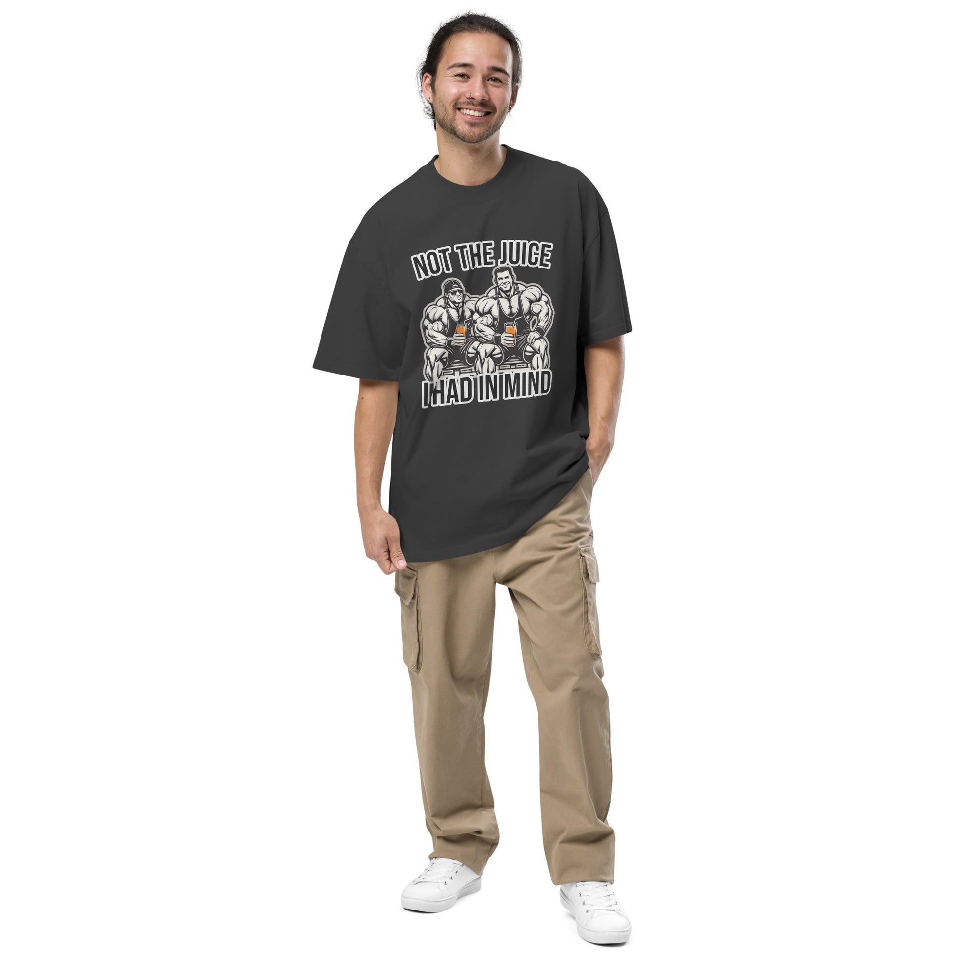 A smiling individual with long hair models Bougie Boiz Clubs Not The Juice - Oversized Faded T-shirt, featuring bodybuilders and the text Not the Juice I Had in Mind, paired with beige cargo pants and white sneakers, against a plain white backdrop.