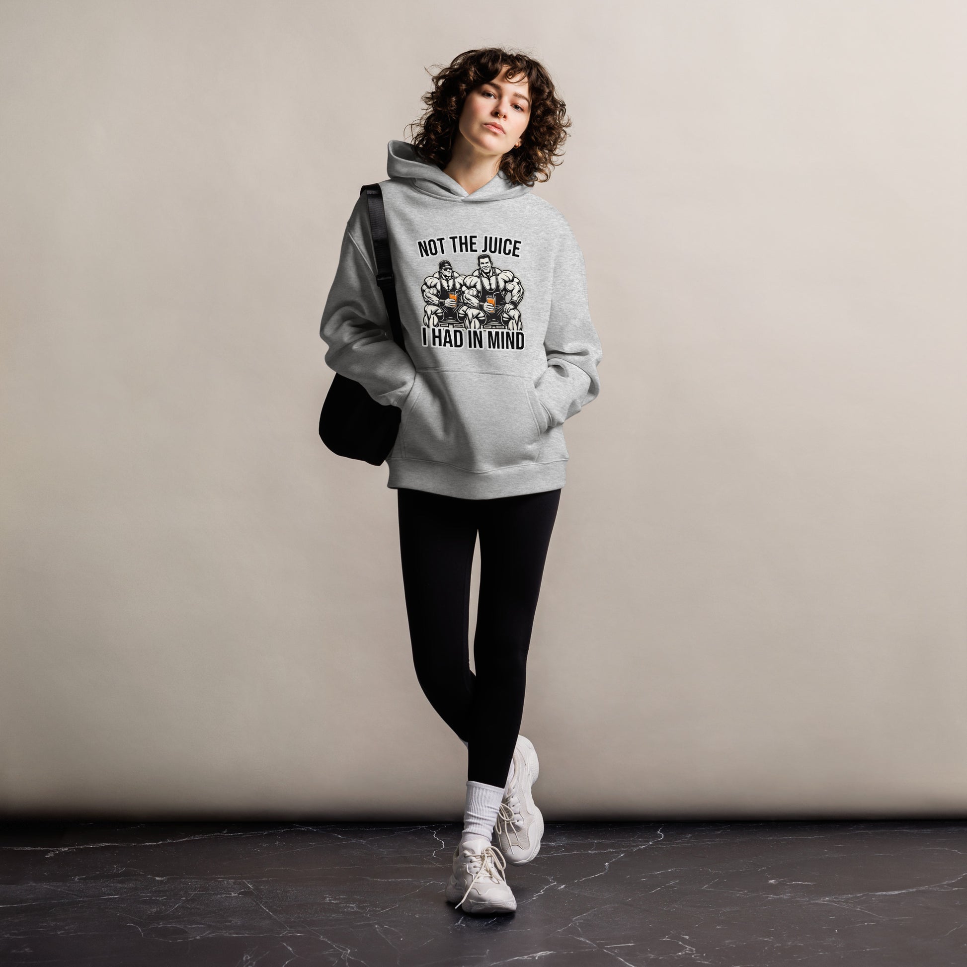 A man wearing Bougie Boiz Clubs Not The Juice - Unisex Oversized Hoodie, featuring two knights with goblets and gym humor text, complements khaki cargo pants. This relaxed fit stands out against a plain white background.