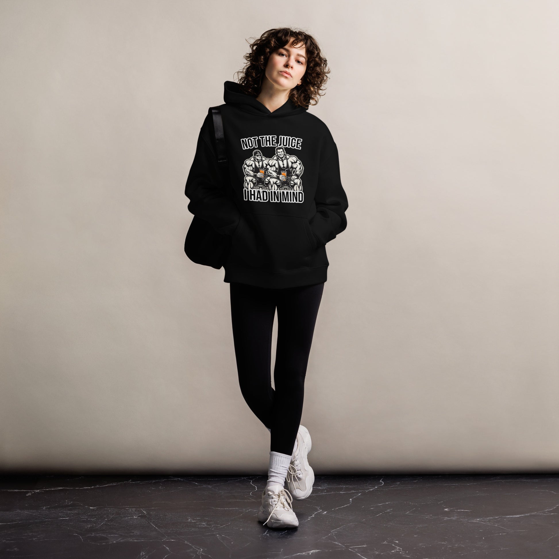 A man wearing Bougie Boiz Clubs Not The Juice - Unisex Oversized Hoodie, featuring two knights with goblets and gym humor text, complements khaki cargo pants. This relaxed fit stands out against a plain white background.