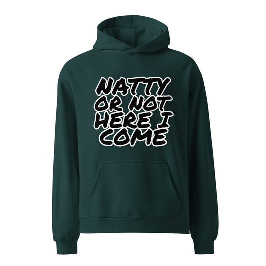 A man sits on a stool against a plain wall, wearing a Bougie Boiz Club Natty Or Not - Unisex Oversized Hoodie with the text READY OR NOT, HERE I COME. The fit complements his black shorts, white socks, and sneakers. The floor beneath displays a subtle marble pattern.