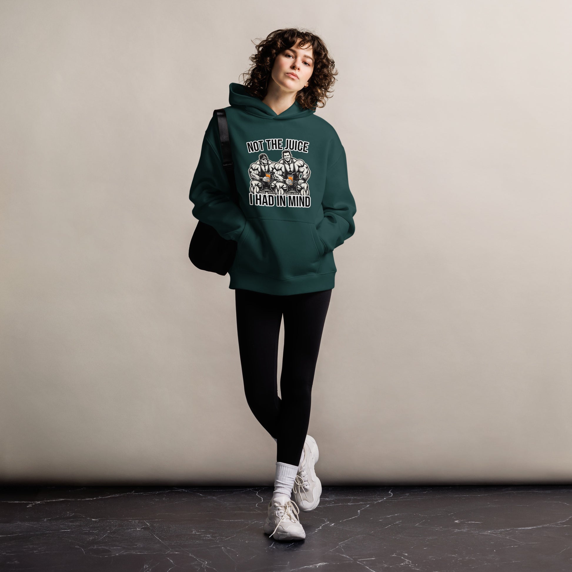 A man wearing Bougie Boiz Clubs Not The Juice - Unisex Oversized Hoodie, featuring two knights with goblets and gym humor text, complements khaki cargo pants. This relaxed fit stands out against a plain white background.