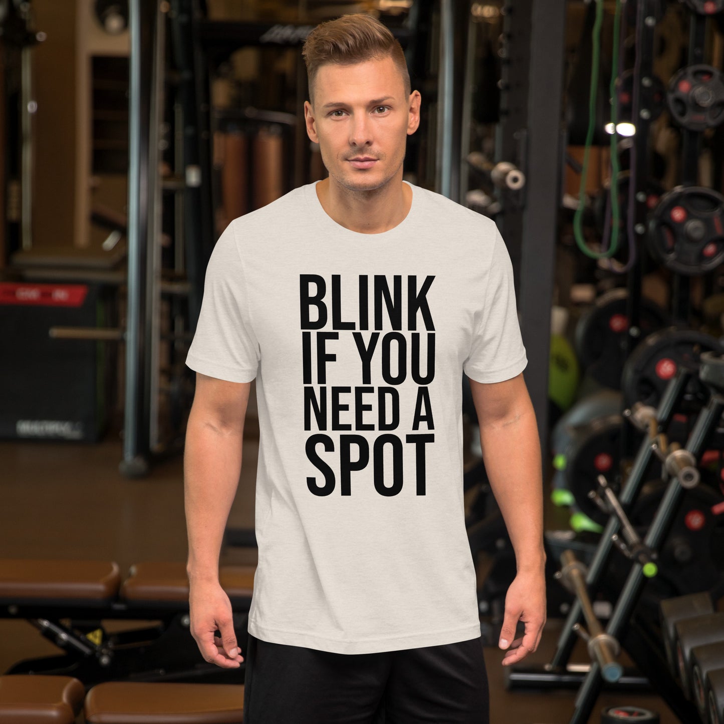 In the gym, a person wears the Bougie Boiz Club Blink If You Need A Spot Unisex T-shirt, highlighted amid weightlifting benches and exercise gear, perfectly setting off this quirky tee.