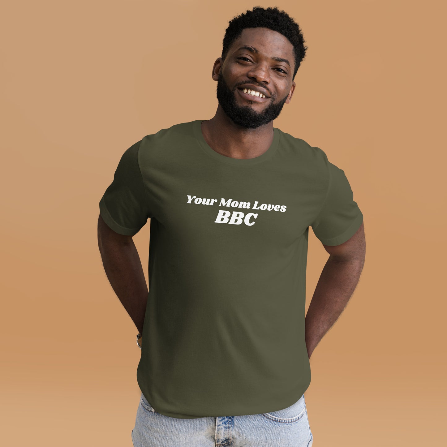 A smiling man combines humor and style in a navy Your Mom Loves BBC unisex T-shirt by Bougie Boiz Club, posing casually with hands in pockets against a neutral brown background. Ideal for gym or casual hangs, this look is both playful and relaxed.