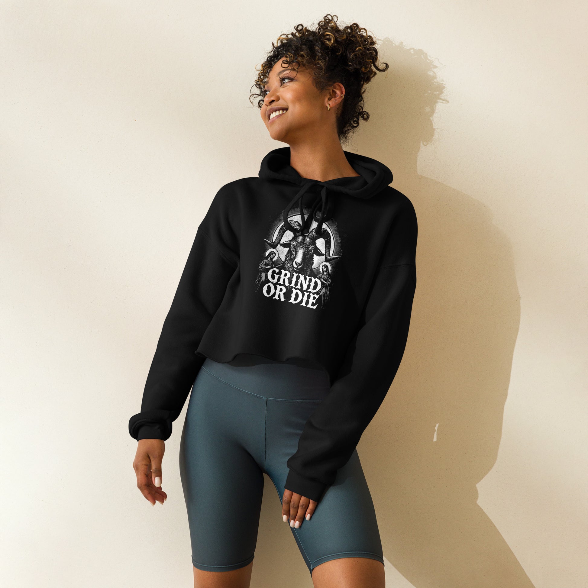 A woman in a Bougie Boiz Club Grind Or Die Womens Crop Hoodie stands confidently, her curly hair framing her face. With one hand on her hip, she gazes upward with a slight smile.